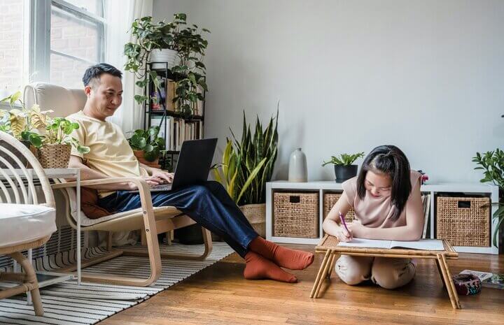 Father studying at home beside daughter quietly colouring book