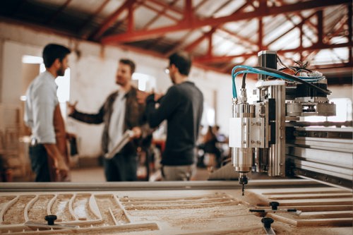 A close up on a woodwork machine with three men in soft focus in the background