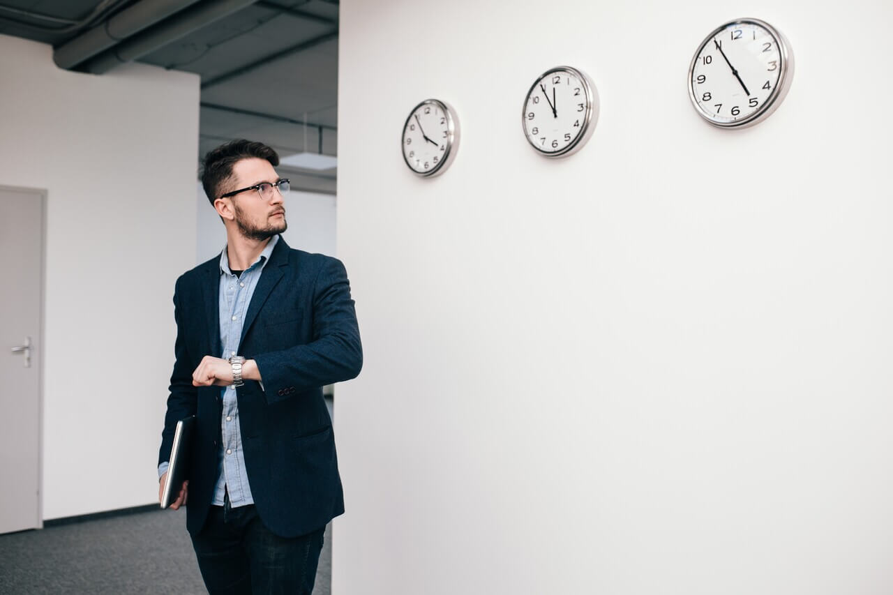 Young man looking at different clocks on a wall, considering his professional skills