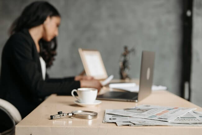 Woman in the background watching her online lessons with a cup of coffee.