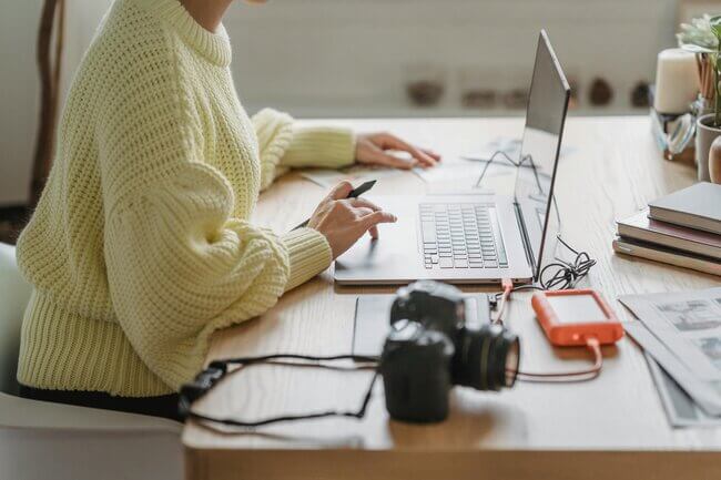 Woman in yellow knit jumper scrolling on her laptop