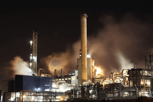 A powerplant at night shrouded in smoke and emissions